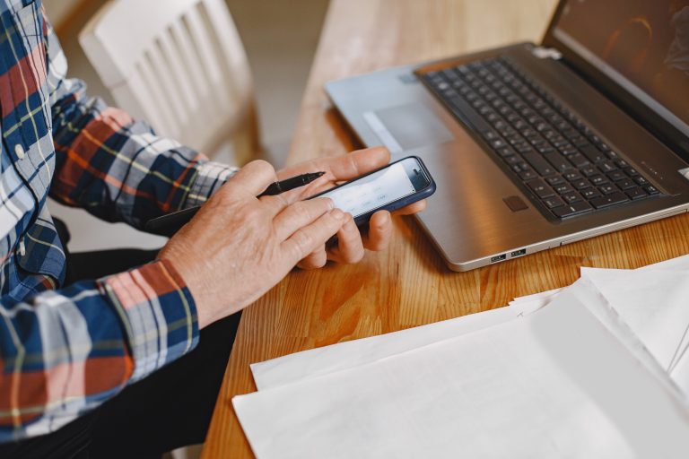 Senior homeowner using a laptop and phone at home for a remote closing